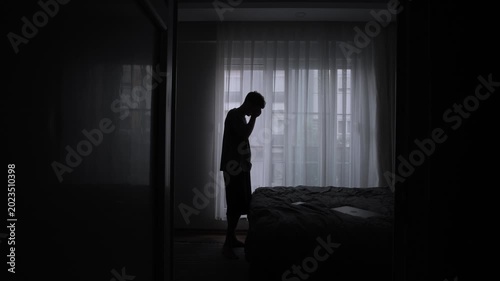 Stressed traveler standing in dark apartment doorway feeling homesick emotionally overwhelmed and exhausted from constant relocation and lonely temporary living