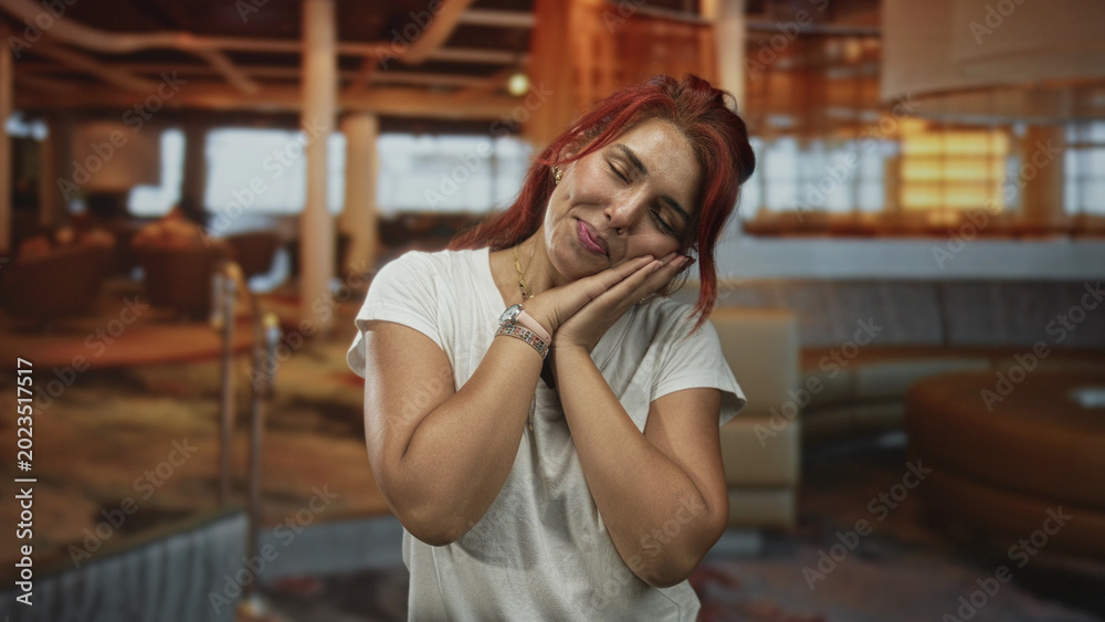 Fototapeta premium Young woman smiling and clapping hands then resting head on palms in restaurant lounge with warm lighting; joy relaxation.
