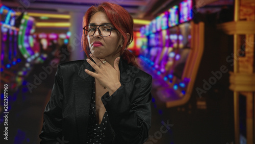 Принти на полотні Woman with red hair and glasses touching cheek beside slot machines in a casino building; disappointment risk isolation