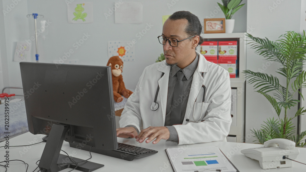Naklejka premium Man doctor types on keyboard while reviewing charts at a computer in a pediatric exam room building; focused care documentation.