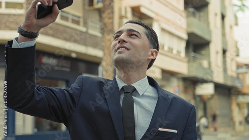 Foto Man in suit raises smartphone aloft on street, holding phone above head while gazing upward; confidence ambition drive