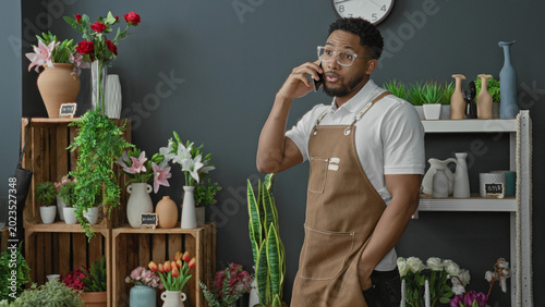 Foto Man florist in brown apron holds smartphone to ear in a studio filled with flowers and plants; attentive service
