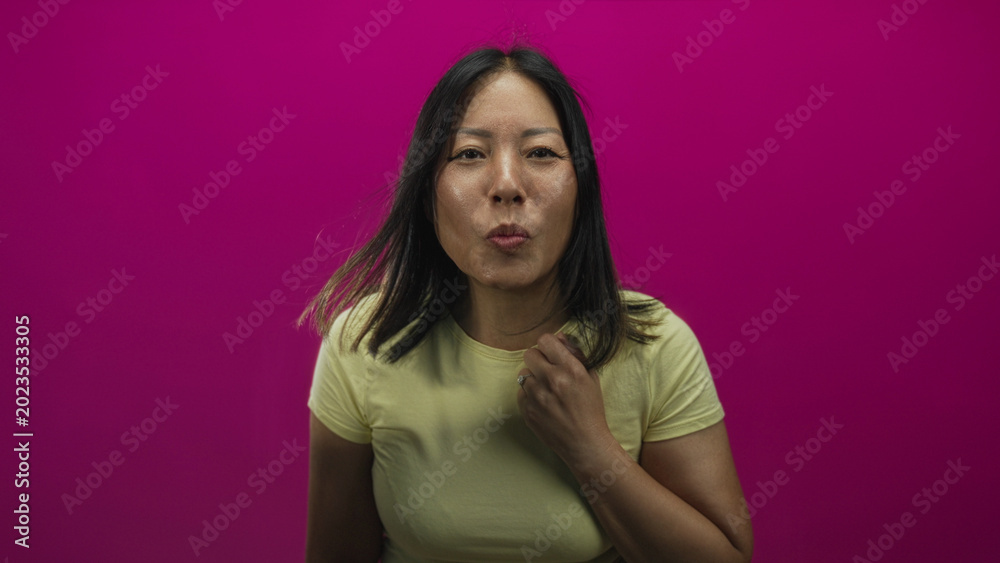 Fototapeta premium Young hispanic woman points index fingers forward toward camera in studio against magenta wall while wearing yellow t shirt; playful confidence.