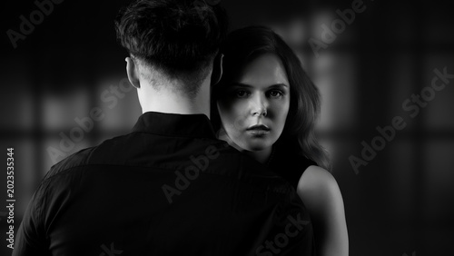 Schilderij op canvas Woman's intense gaze from behind a man's back, conveying mystery and intrigue