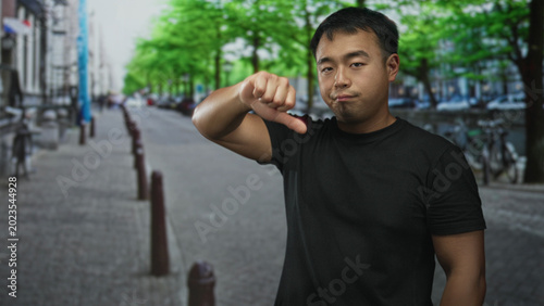 Photos Man in black t shirt showing thumbs down with hand on street lined with bicycles and green trees; disapproval
