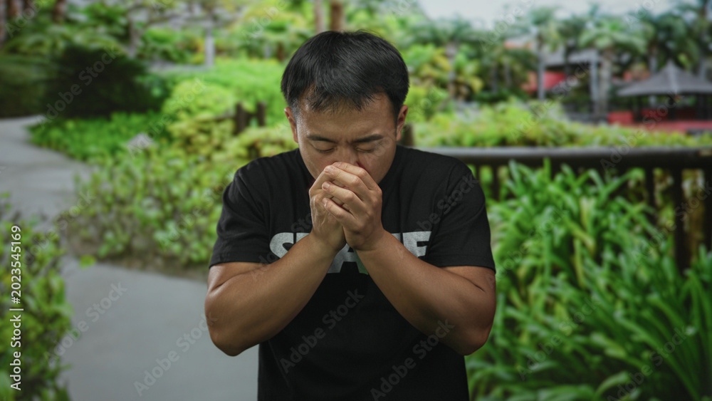 Fototapeta premium Man clutch chest for heartattack while standing in green forest pathway surrounded by lush foliage; health danger distress.