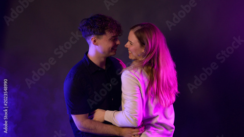 Young couple embracing and laughing together under blue and pink neon lighting