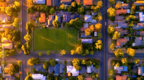 Aerial view of a vibrant neighborhood with illuminated houses and a green soccer field at sunset