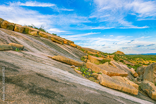 Fractured slabs of pink granite slide down the massive dome's steep slopes under a sweeping blue sky in Texas Hill Country