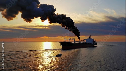 A cargo ship emits smoke while sailing across the ocean during a beautiful sunset video