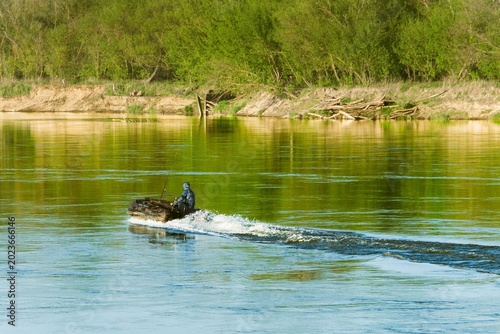 A horizontal photo of a man sailing a motorboat down a river.