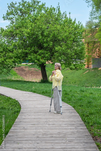 An adult attractive woman walks in the park on crutches after an injury.