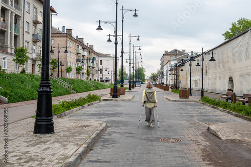An adult attractive woman walks along a city street on crutches after an injury.
