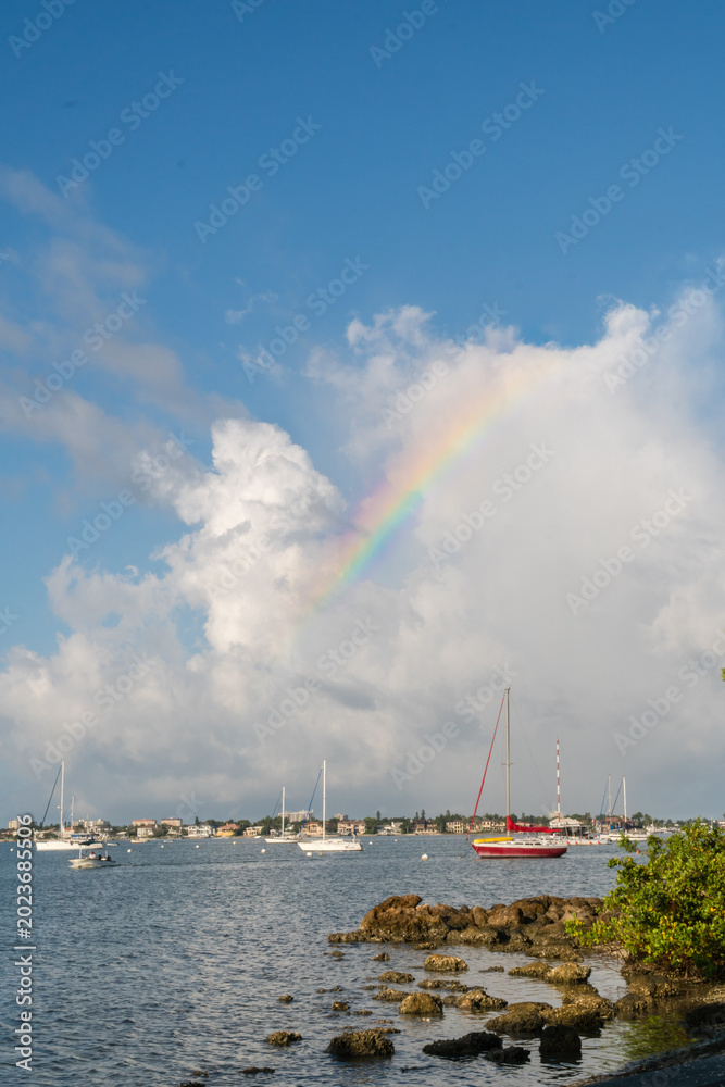 Obraz premium Sailboats in harbor with dramatic clouds and rainbow in sky on sunny day in Sarasota Florida.