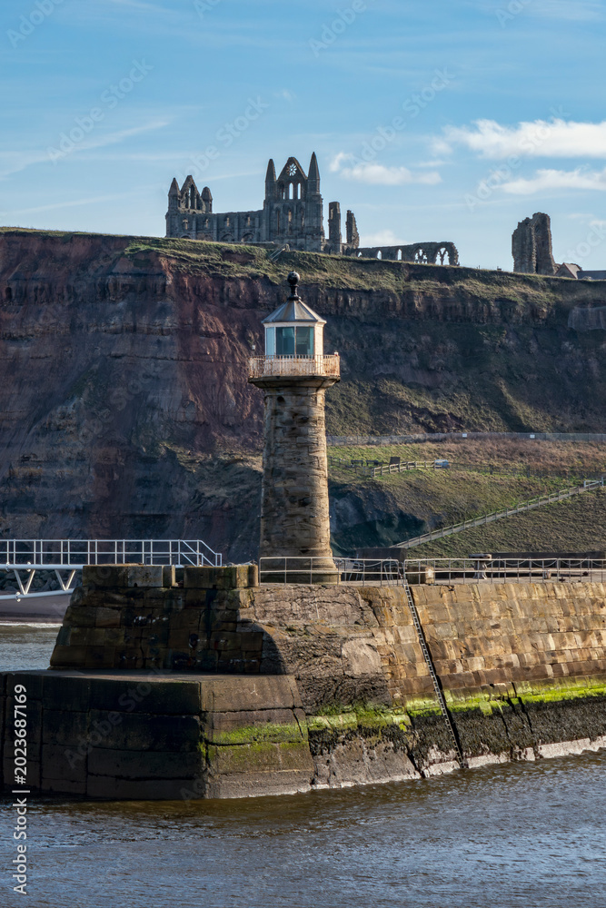 Obraz premium whitby abbey on the cliff top above the east pier lighthouse sunny day low sun no people