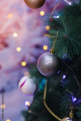 Elegant Christmas ornaments hanging on a glowing pine tree create a warm festive atmosphere with colorful lights, soft bokeh, and cozy holiday vibes perfect for seasonal backgrounds in wintertime. 4k.