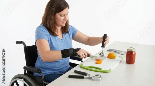 Woman in wheelchair using adaptive kitchen tools to prepare healthy food on white tabletop isolated on white background