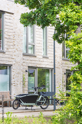 Electric cargo bike parked outside suburban brick house in Ede, Netherlands under leafy trees