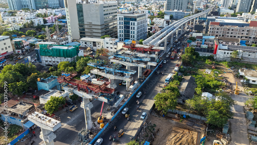 Fototapeta premium Aerial view of metro rail construction over busy city road with elevated track and urban buildings showing infrastructure development and public transport expansion