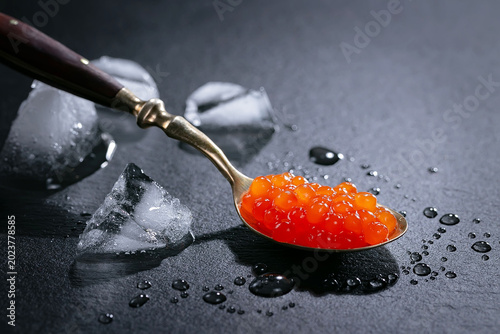 Red caviar, a healthy and tasty seafood product, in a spoon, on a dark background.