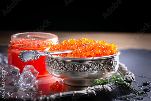 Red, granular caviar, a tasty, valuable product in a spoon and silverware on a black background. Close-up.
