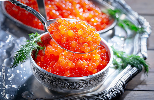 Red, granular caviar, a tasty, valuable product in a spoon and silverware on a black background. Close-up.