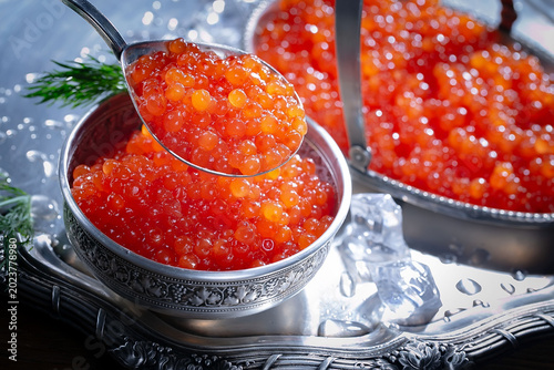 Red, granular caviar, a tasty, valuable product in a spoon and silverware on a black background. Close-up.