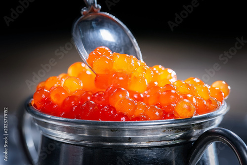 Red, granular caviar, a tasty, valuable product in a spoon and silverware on a black background. Close-up.