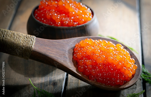 Red, granular caviar, a tasty, valuable product in a spoon and silverware on a black background. Close-up.