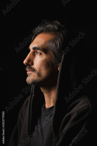 Man in a dark hoodie gazes thoughtfully into the shadows at night