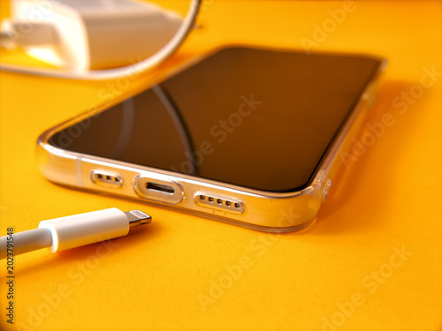 Close-up shot a white mobile phone data cable near a smartphone device on a bright yellow-orange surface