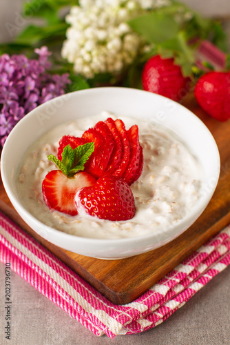 Healthy breakfast with yogurt, strawberries, oats in a decoration with colorful lilac flowers	