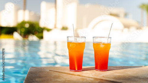 Two vibrant cocktails sit by a sunlit poolside