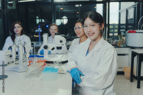 Fotografi Diverse female researchers in lab coats and safety glasses smiling, standing wit
