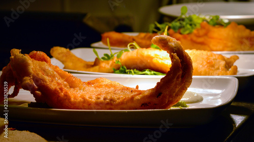 Schilderij op canvas British deep fried battered fish fillets with green herbs on white plates in a restaurant