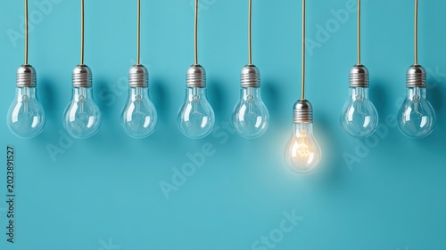 青い背景に吊るされた複数の電球のうち一つだけが点灯している状態。アイデアやひらめきの象徴としてビジネスやプレゼンテーションに使えるイメージ素材