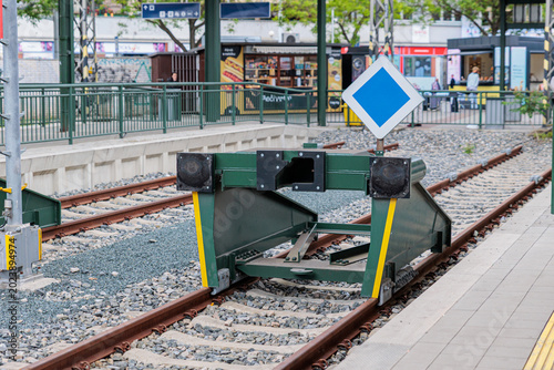 Tablou pe pânză Green Railway Buffer Stop at Urban Train Platform With Blue Priority Sign and En
