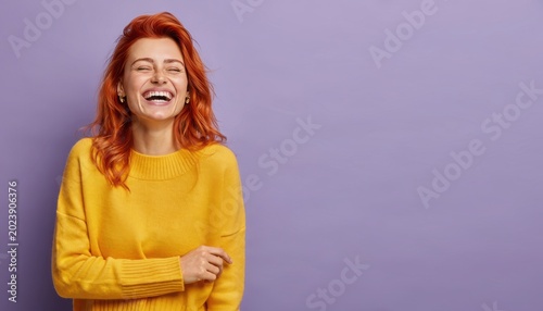 Happy Woman with Red Hair Laughing Brightly in Yellow Sweater against Purple Background