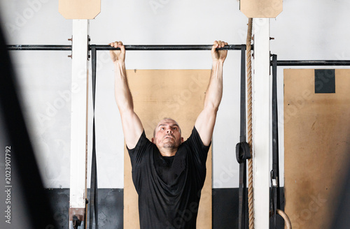 Male athlete building upper body strength, hanging from a pull up bar during an intense workout session in a gym