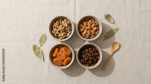 Healthy dried fruit and nut selection arranged in minimalist bowls on a neutral textured linen background with natural sunlight creating gentle shadows for a calm culinary presentation