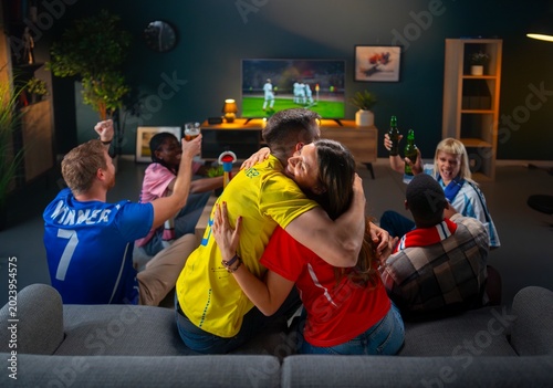 Foto A group of friends gathers in a living room to watch a soccer match on TV