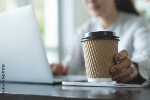 Business woman hand holding a paper cup of coffee during working on laptop at home office or modern workspace,. taking a break, freelance at work