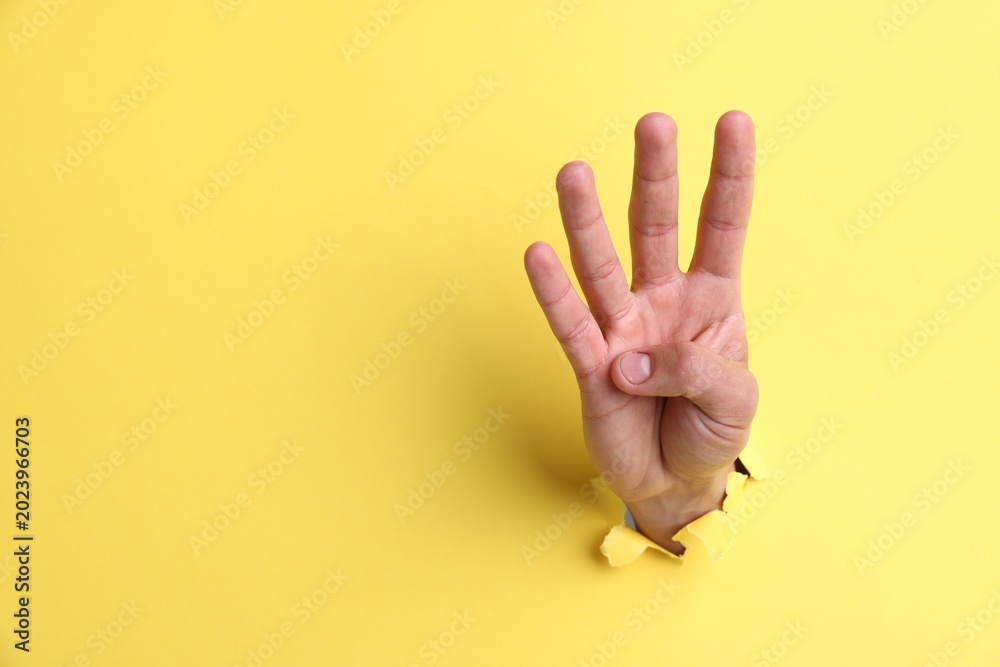 Naklejka premium Man showing number four with fingers through hole in yellow paper, closeup. Space for text
