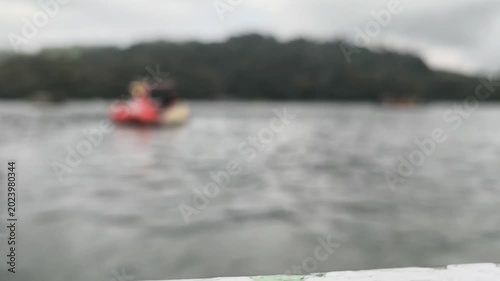 Blurred close-up shot of a person kayaking or paddling on a lake. Soft focus effect emphasizes motion and the tranquil waterside environment