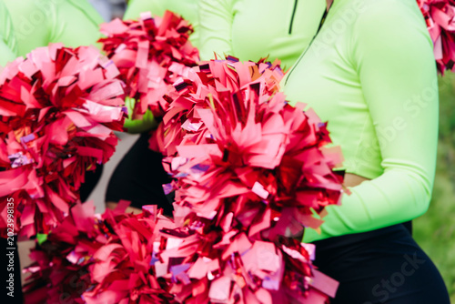 Female cheerleaders group in action, pink and green uniform with pom-pom, audience and sport teams in the background, performing and supporting during outdoor game match, cheerleading on stadium
