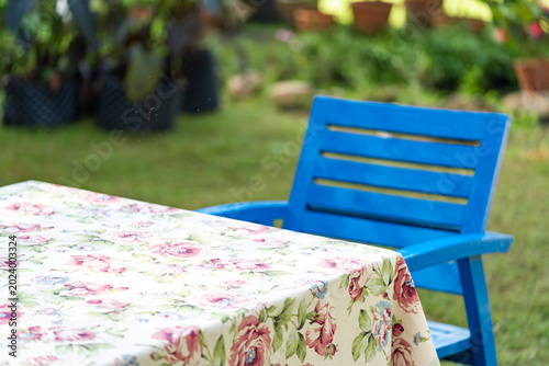Schilderij op canvas Blue wooden chairs and floral tablecloth arranged in green garden for relaxing outdoor seating atmosphere