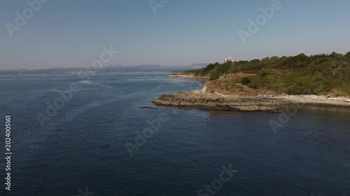 Drone footage flying along a beautiful ocean coastline with a historic fort on the hills.