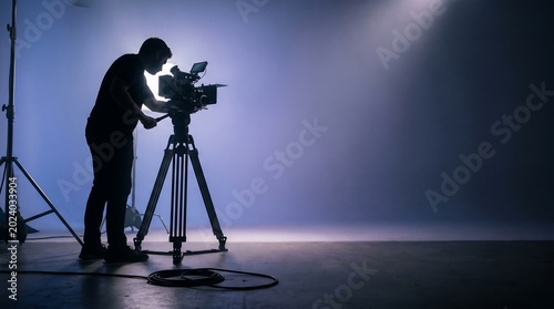 Filmmaker operating camera in studio for media productions, ideal BTS shot for news and advertising with excellent copy space.
