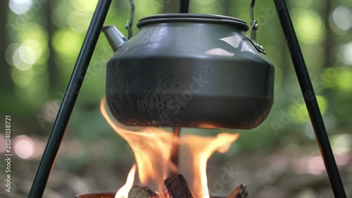 Boiling water in a black kettle over an open campfire in the woods.