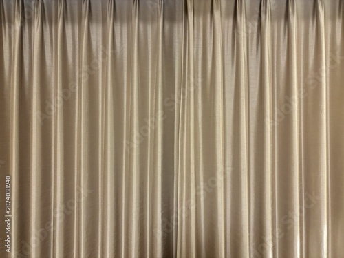 Full frame background of an elegant beige curtain fabric featuring beautiful vertical pleats and soft folds, showing smooth silky texture with gentle highlights and interior shadows